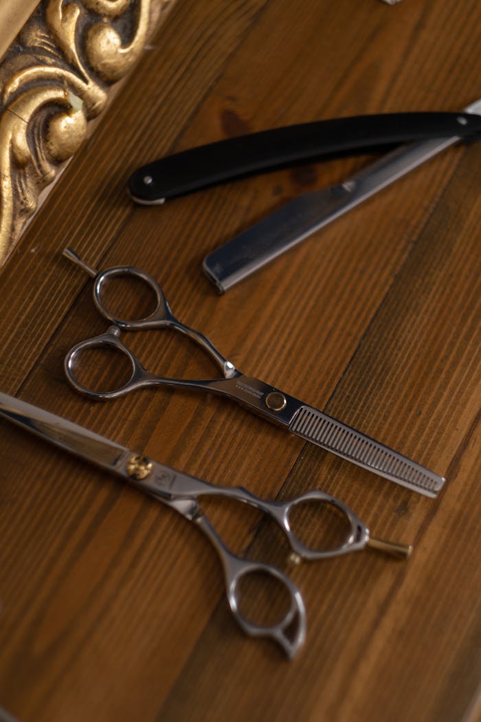 A flat lay of scissors and straight razor on a wooden table, ideal for barbershop themes.